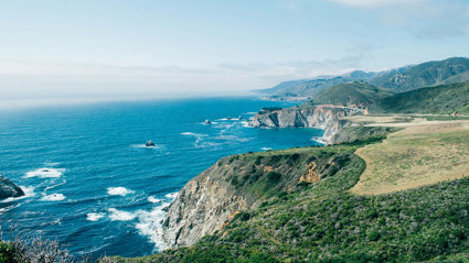 Cliffs covered in vegetation by the sea under a clear sky.