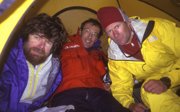 Three expeditioners in winter gear resting inside a tent.