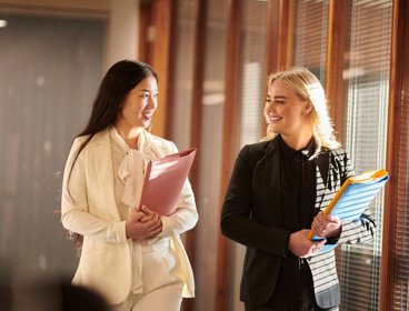 Two professionals in suits and holding folders walking.
