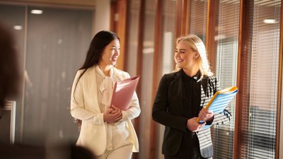 Two professionals in suits and holding folders walking.