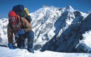 Expeditioner in winter gear climbing over the edge of a glacier.