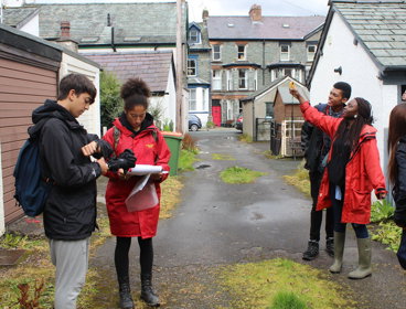 Group of young people taking measurements in a lane behind a row of houses.