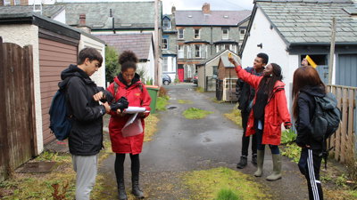 Group of young people taking measurements in a lane behind a row of houses.