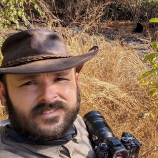 Kevin Murphy wearing a brown leather hat, in a grassy field with a camera.