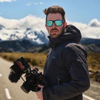 Person holding camera in outdoor setting against mountain background.