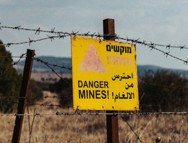 Yellow danger sign warning of mines, attached to barbed wire fence.