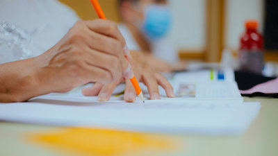 Close-up of a person writing something on paper using a pencil. 
