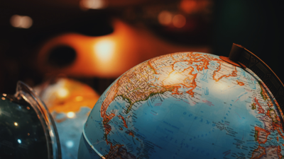 Several globes sit on a table in a dimly lit room. One sits in the foreground showing the northern portion of the weastern hemisphere whilst the rest remain blurred in the background.