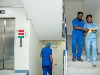 Two health professionals dressed in blue uniforms walking down a flight of stairs, looking at some documents and talking