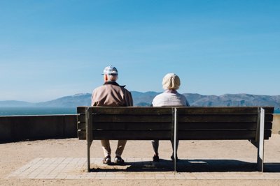 Two people sitting on a bench looking out onto sea and mountains
