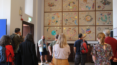 Hormazd Narielwalla in front of his artwork, Expanding Universe, in the RGS Map Room. He is delivering a talk to an audience.