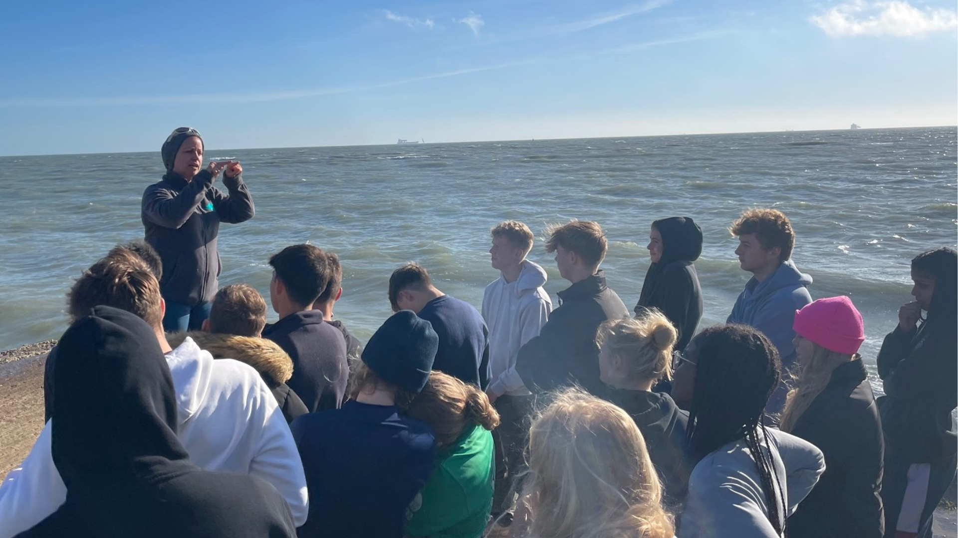 Chloë Searl speaking to group of students on the beach next to the sea.