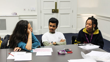 Three people sitting, with one person talking and the two others listening attentively. 