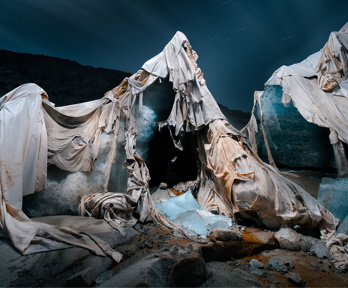 Torn thermally reflective blankets used as coverings draped around pieced of ice on a glacier.