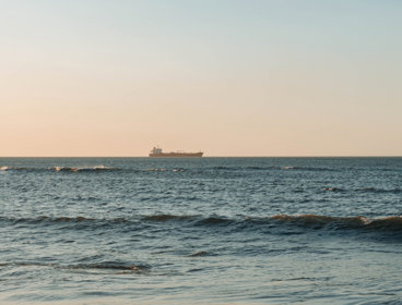 A container ship sailing on the calm sea horizon, captured at dawn.