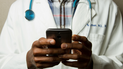 A doctor stands in their lab coat as they type on their phone