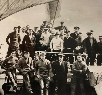 A sepia image of Ernest Shackleton and the crew of Endurance, standing on the ship with sails in the background