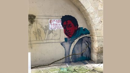 Street art of a person in a blue jacket painted on a stone wall under an archway with a sign in French.