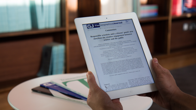 Hands holding a tablet showing an article in The Geographical Journal on the screen
