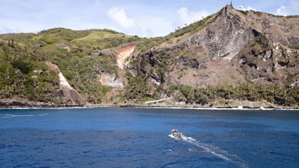 A coastal cliff landscape covered in grassy vegetation with a motor boat moving towards the cliffs.