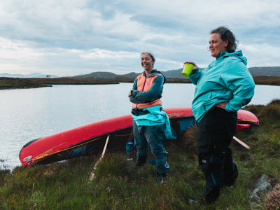 Two people standing with a canoe by water