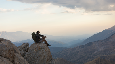 Backpacker sitting on a rock looking at the view of a mountain range.