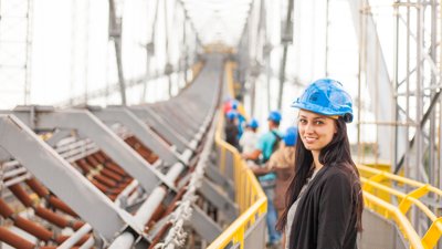 Woman with long, dark hair smiling and wearing blue hard hat in construction setting