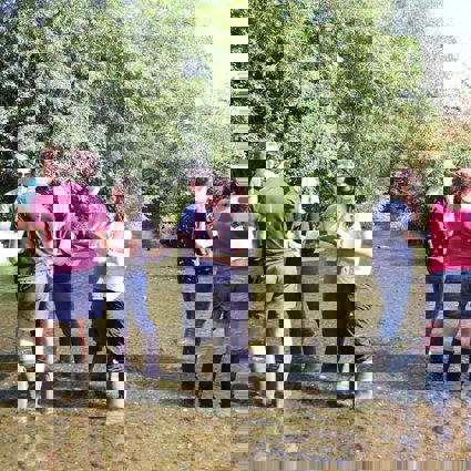 A group of teachers are standing in a shallow river, looking at clipboards