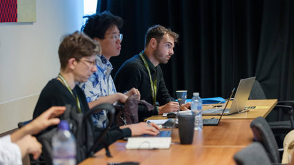 Three conference delegates seated and listening to a conference presentation.