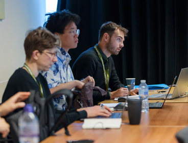 Three conference delegates seated and listening to a conference presentation.