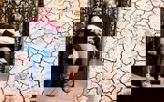 A woman sitting in a chair on the left and a cracked dry cracked river bed on the right.