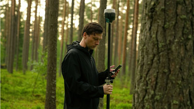 Person in a black raincoat carrying out land surveying research in the woods.