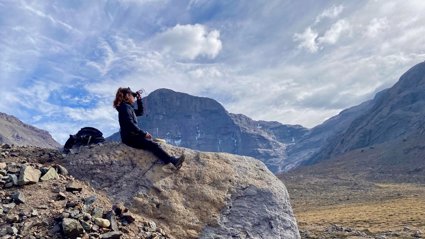 Person sat on a rock looking out at a mountainous landscape in Chile. The person is holding a compass and has a rucksack beside them.