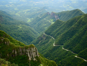 Winding road through steep, green mountains in a lush, forested valley.