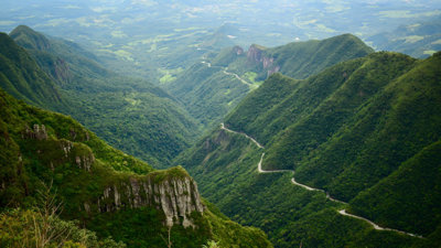 Winding road through steep, green mountains in a lush, forested valley.