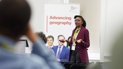 Speaker presenting in front of banner reading 'advancing geography'