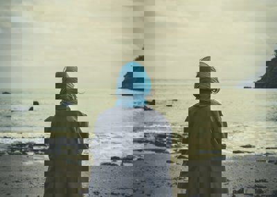 A person with a blue scarf and grey jacket looks out onto the sea