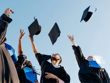 Students throwing graduation hats into blue sky.