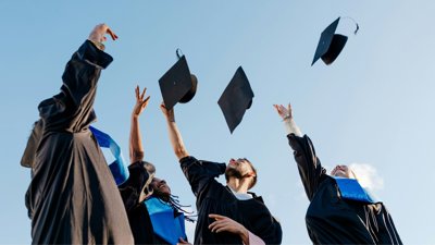 Students throwing graduation hats into blue sky.
