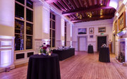 Poseur tables with floral arrangements and candles set-up for a drinks reception in a grand main hall. 