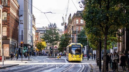 A busy town centre road with a yellow tram driving along.