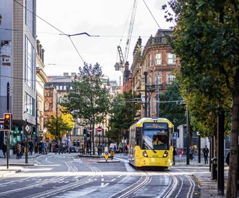 A busy town centre road with a yellow tram driving along.