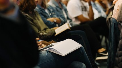 Close up view of people sitting in a row with notebooks on their lap.
