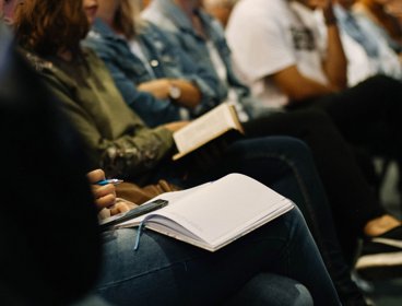 Close up view of people sitting in a row with notebooks on their lap.