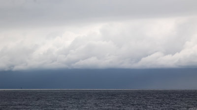 A seascape with white fluffy clouds over a grey sea