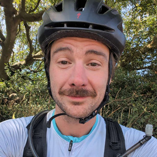 A selfie of Tom Weiser in a forest, wearing a cycling helmet