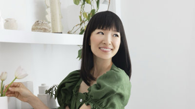 Marie Kondo wearing green top against clean white interior background.