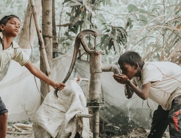 Indian boys at  water pump, one is drinking