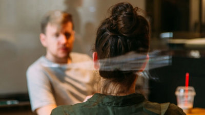 Two people sitting across from each other, with one person seen from behind and the other person blurred. 