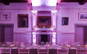 A formal banquet table set-up in a grand main hall with pink uplighters. 